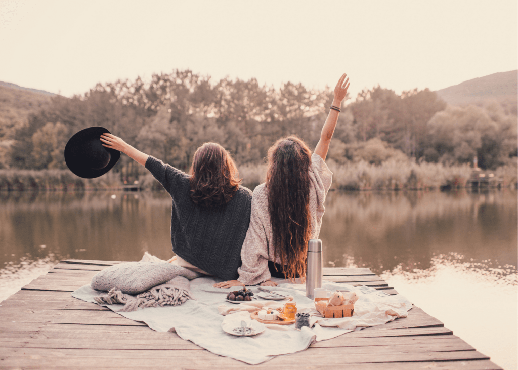 Two women having picnic in forest by lake